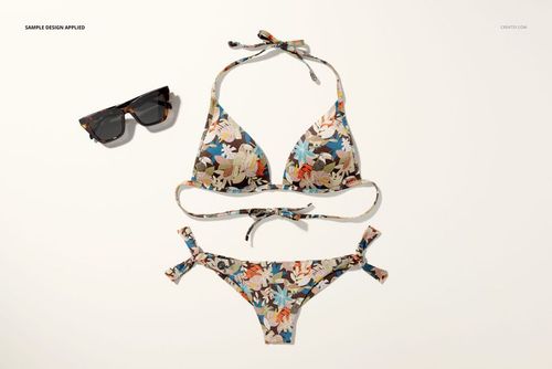 PSD mockup of a bikini set featuring a multicolor floral print, arranged beside sunglasses on a pale surface.