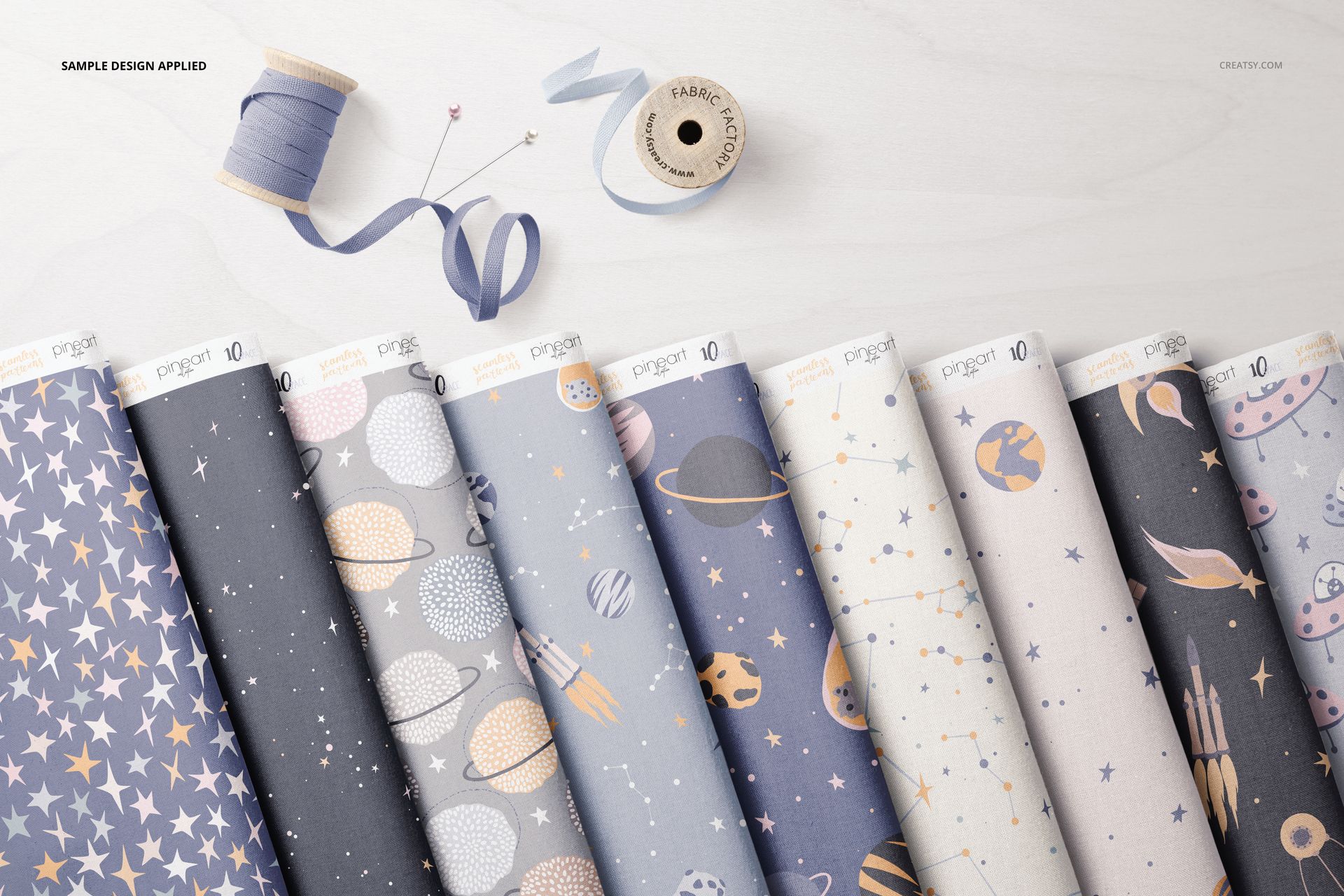 PSD mockup showing multiple folded fabrics with whimsical star and space prints, next to sewing thread and ribbon.