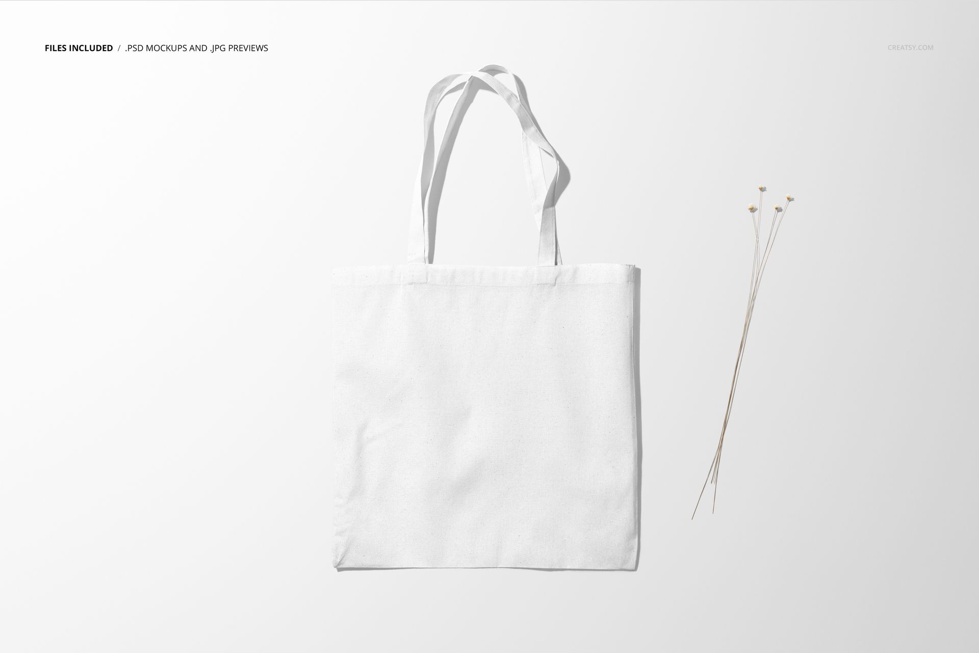 White tote bag mockup displayed from the front, set against a minimal light backdrop with dried stems beside it.