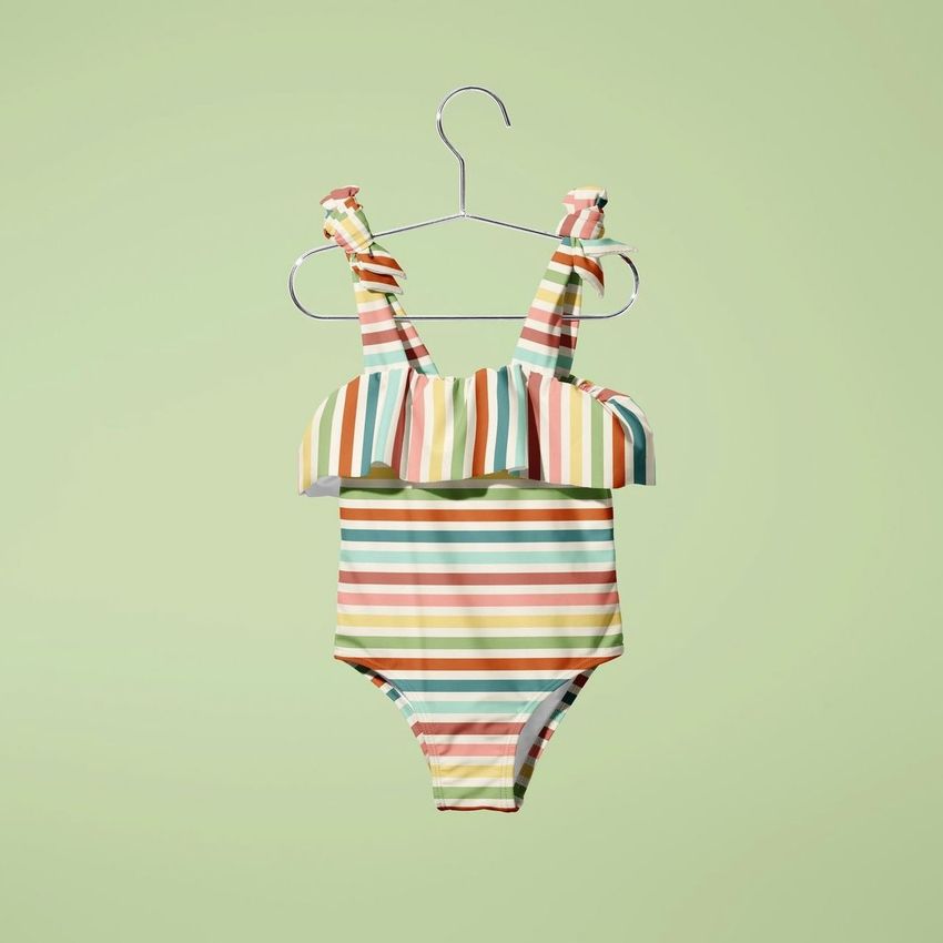 Baby swimsuit mockup featuring a striped one-piece suit with ruffle detail, displayed on a hanger against a light green background.