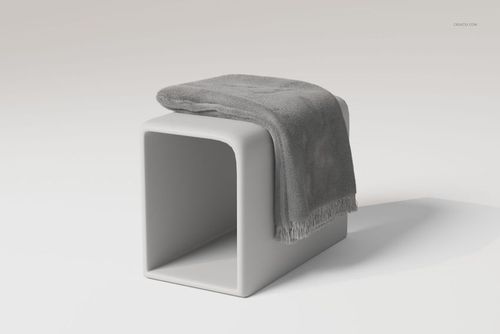 Gray fringe blanket draped over a modern white pedestal, shown in a minimalist setting with soft lighting.