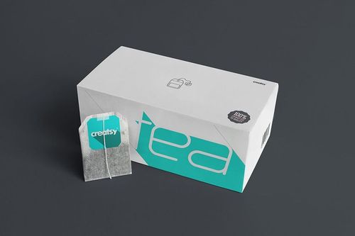 Front view of a tea packaging mockup featuring a white box with teal accents and a visible tea bag beside it.