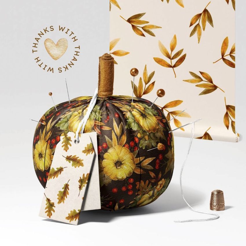 Fabric pumpkin mockup featuring a dark floral-patterned pumpkin with tags, pins, and autumn-themed props on a light background.