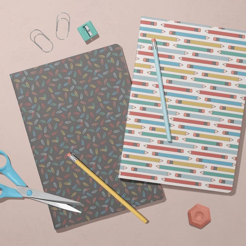 Stationery mockup featuring two classic A4 notebooks with colorful pencil patterns, surrounded by scissors, paper clips, and a pencil on a light surface.