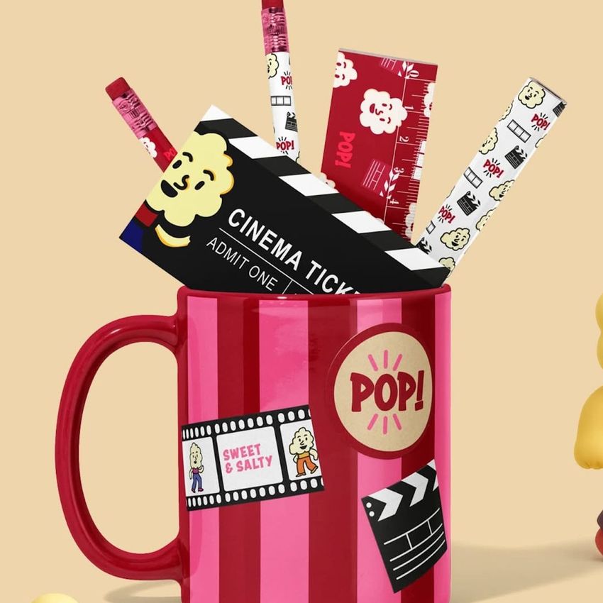 Mug mockup with red and pink stripes, filled with stationery items like pencils, a ruler, and a cinema ticket on a beige background.