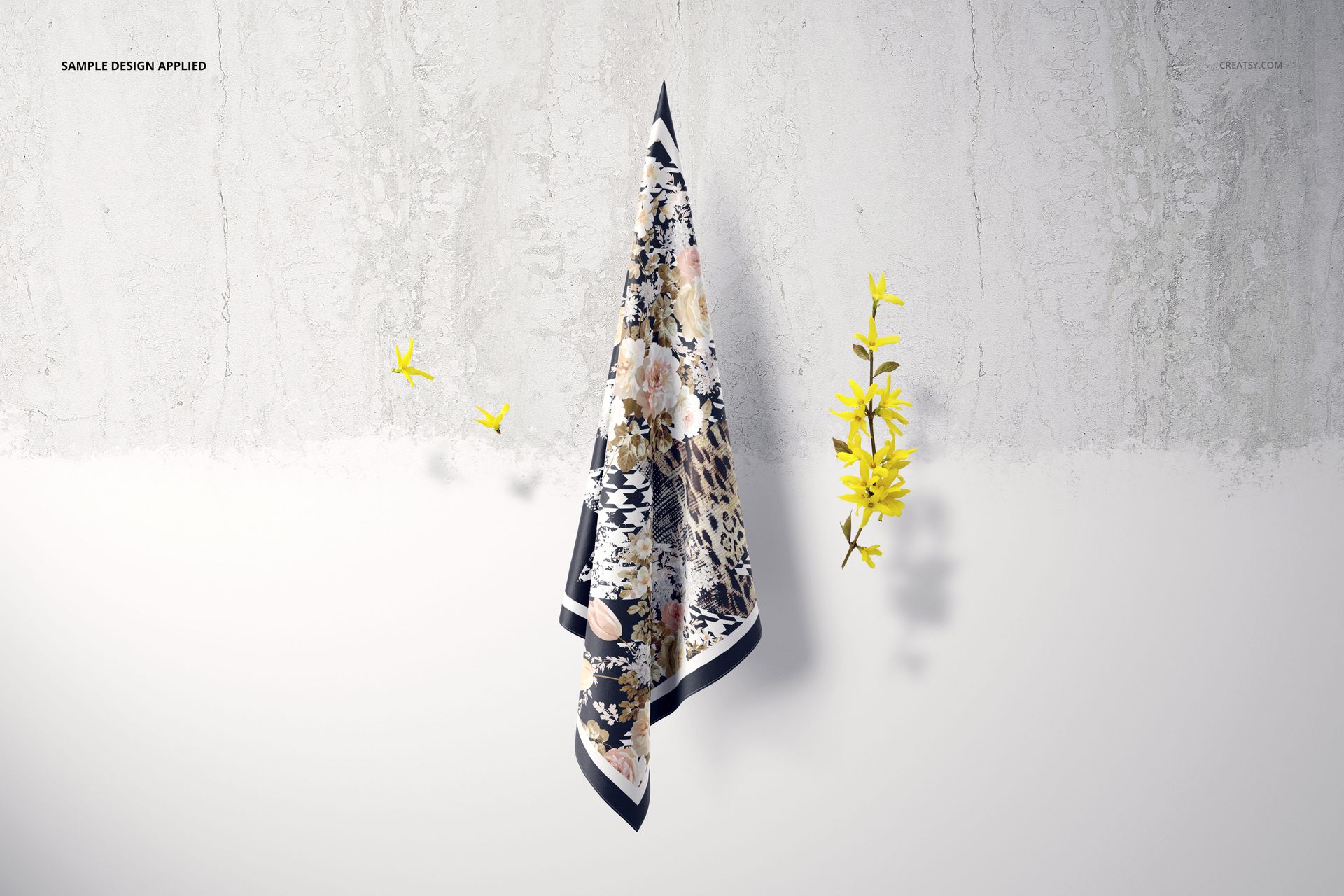 Hanging square silk scarf mockup featuring a patterned fabric draped on a wall, accented by small yellow flowers.