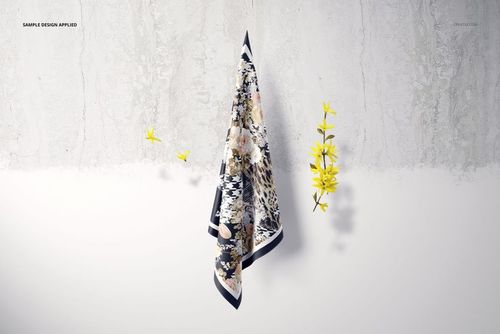 Hanging square silk scarf mockup featuring a patterned fabric draped on a wall, accented by small yellow flowers.