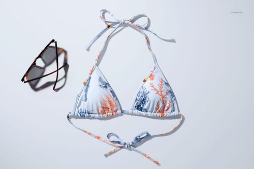 PSD mockup showing a bikini top featuring marine-themed coral pattern, arranged next to sunglasses on a pale backdrop.