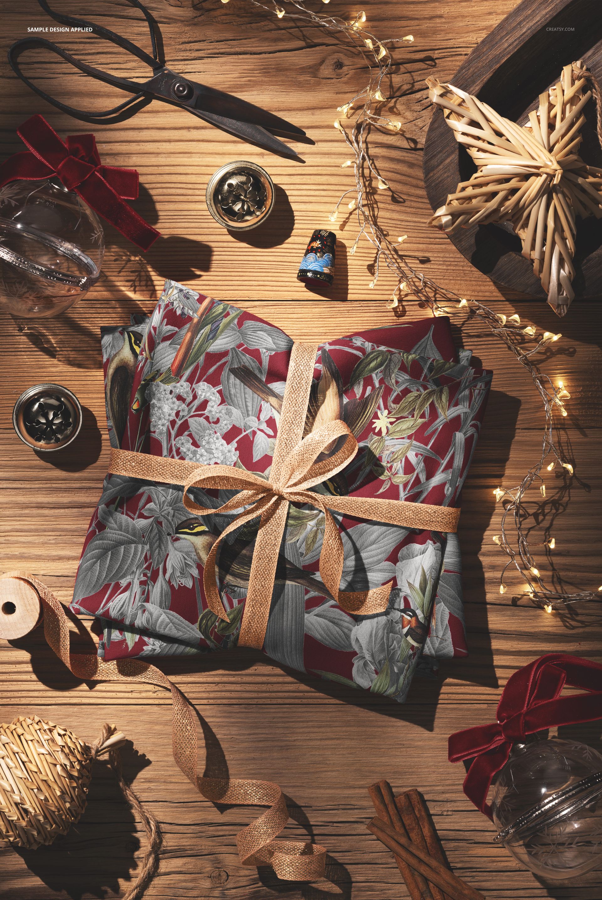 Christmas-themed folded jersey fabric mockup with a ribbon, surrounded by ornaments, fairy lights, and craft supplies.