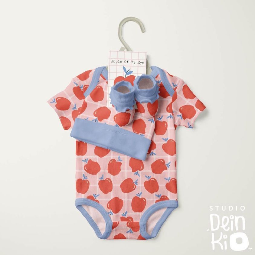 Kids onesie mockup with a red apple pattern, matching blue booties, and headband displayed on a hanger against a light background.
