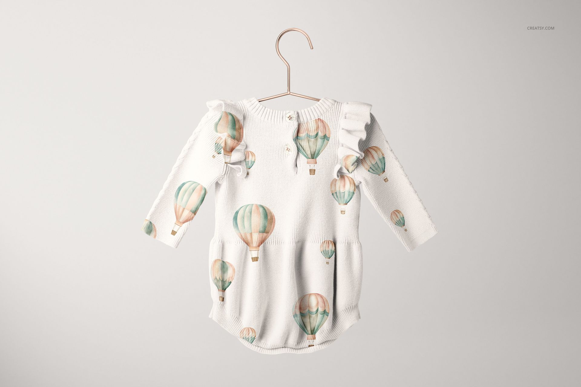Knitted baby romper mockup featuring long sleeves, ruffled shoulders, and pastel hot air balloons, suspended on a hanger.