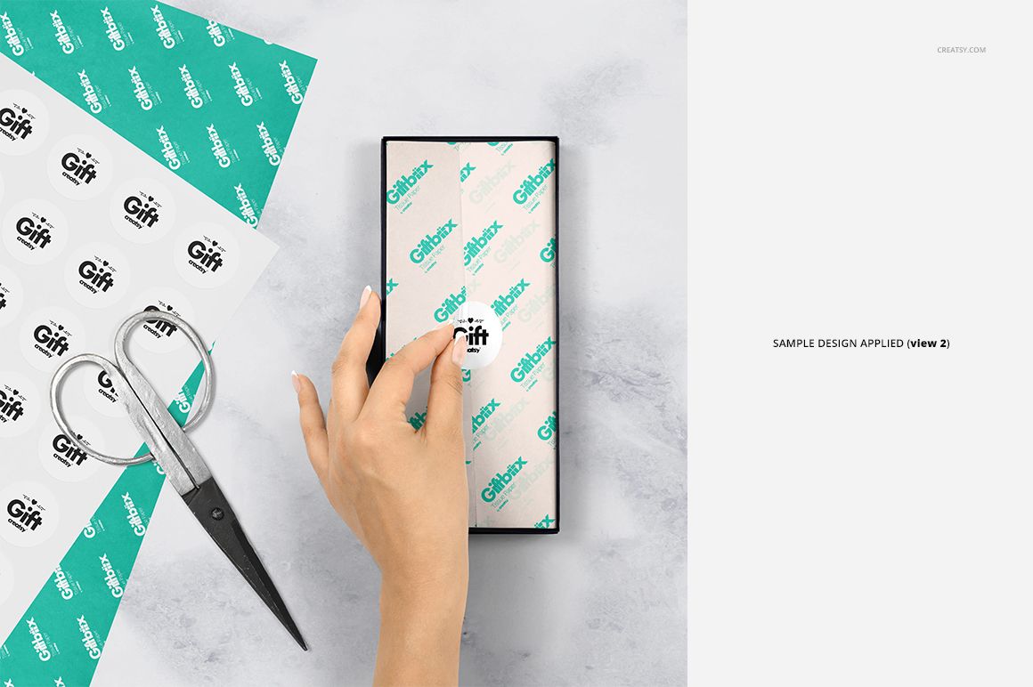 Rectangular gift box on marble surface, covered with printed tissue paper, hand and scissors visible, PSD mockup scene.