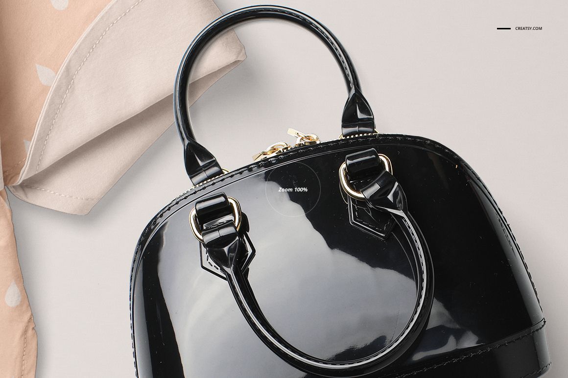 Glossy black handbag mockup showing gold buckles and zipper, partially overlapping a beige polka dot cloth on a neutral background.