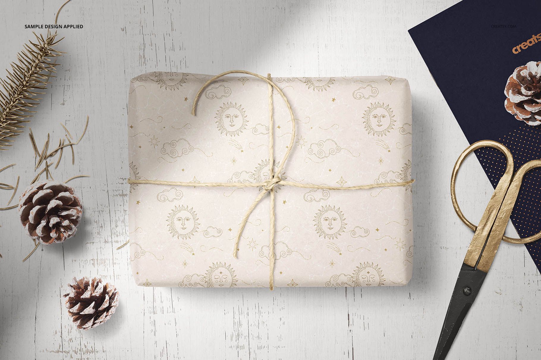 Gift wrapping tissue paper mockup showing a rectangular package with string, pinecones, and scissors nearby.