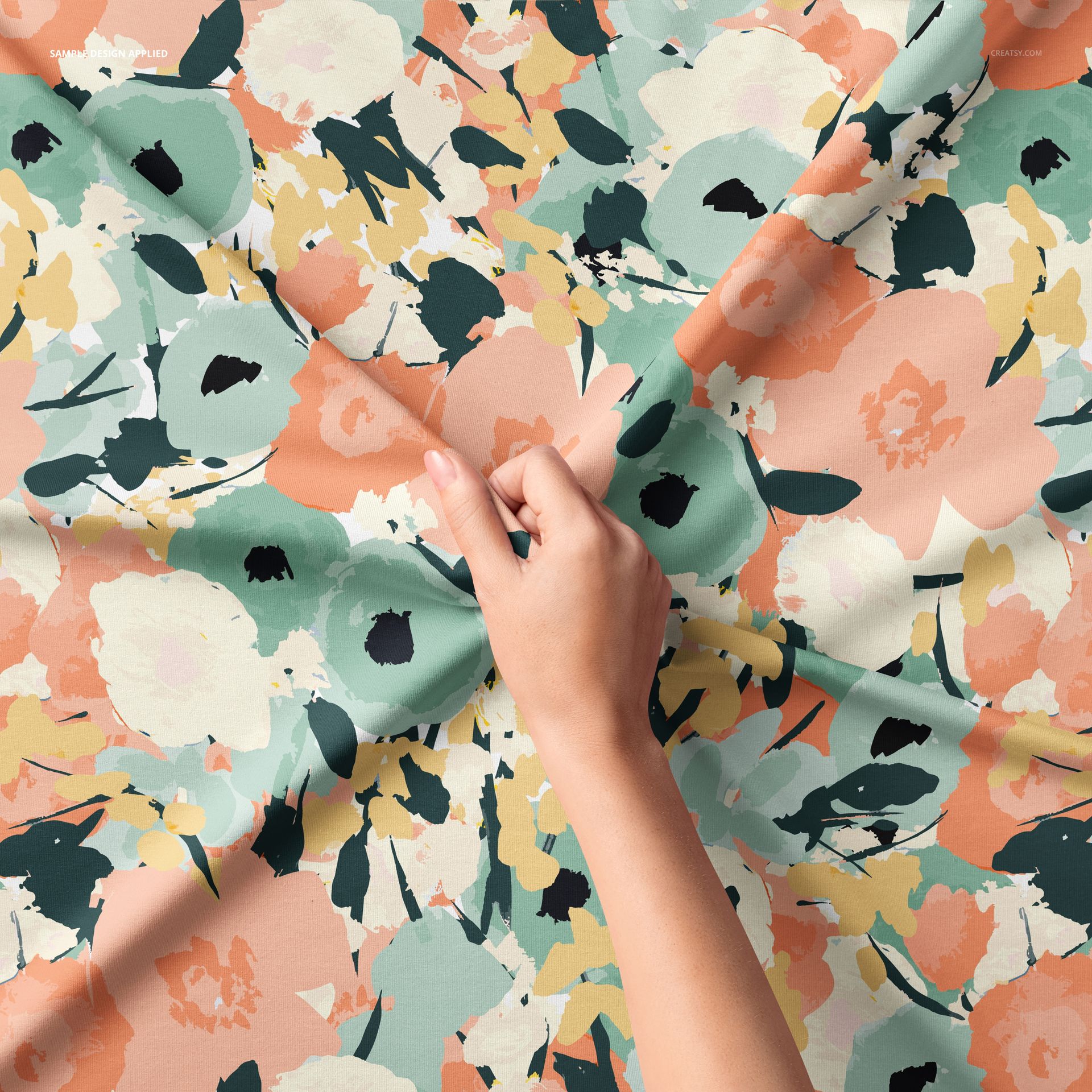 Hand pinching a piece of jersey fabric with a colorful floral pattern, viewed from above in a fabric mockup.