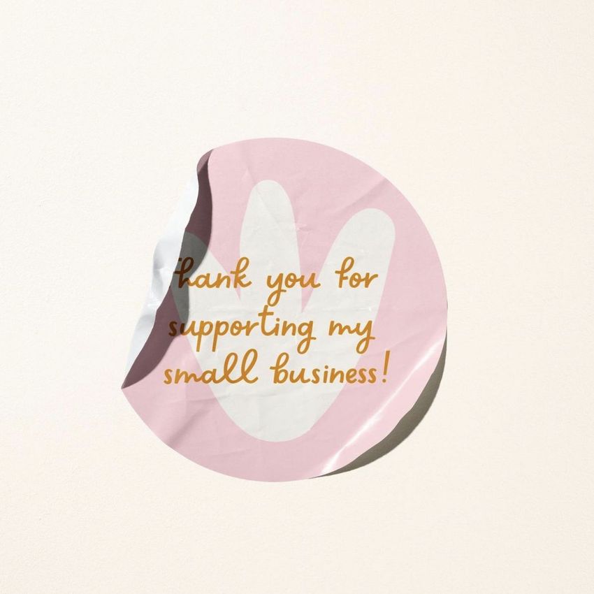 Sticker mockup featuring a round sticker with a pink background and handwritten text, placed on a light beige surface.