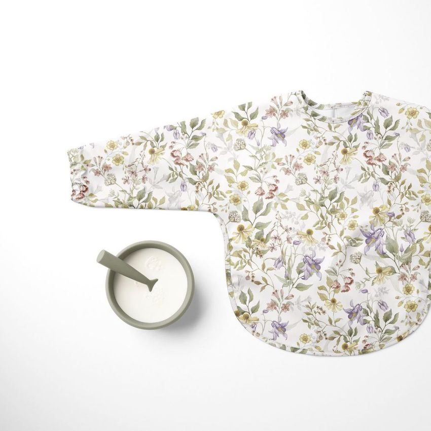 Baby sleeved bib mockup featuring a floral pattern in soft pastel colors, displayed flat on a white surface next to a bowl of milk.