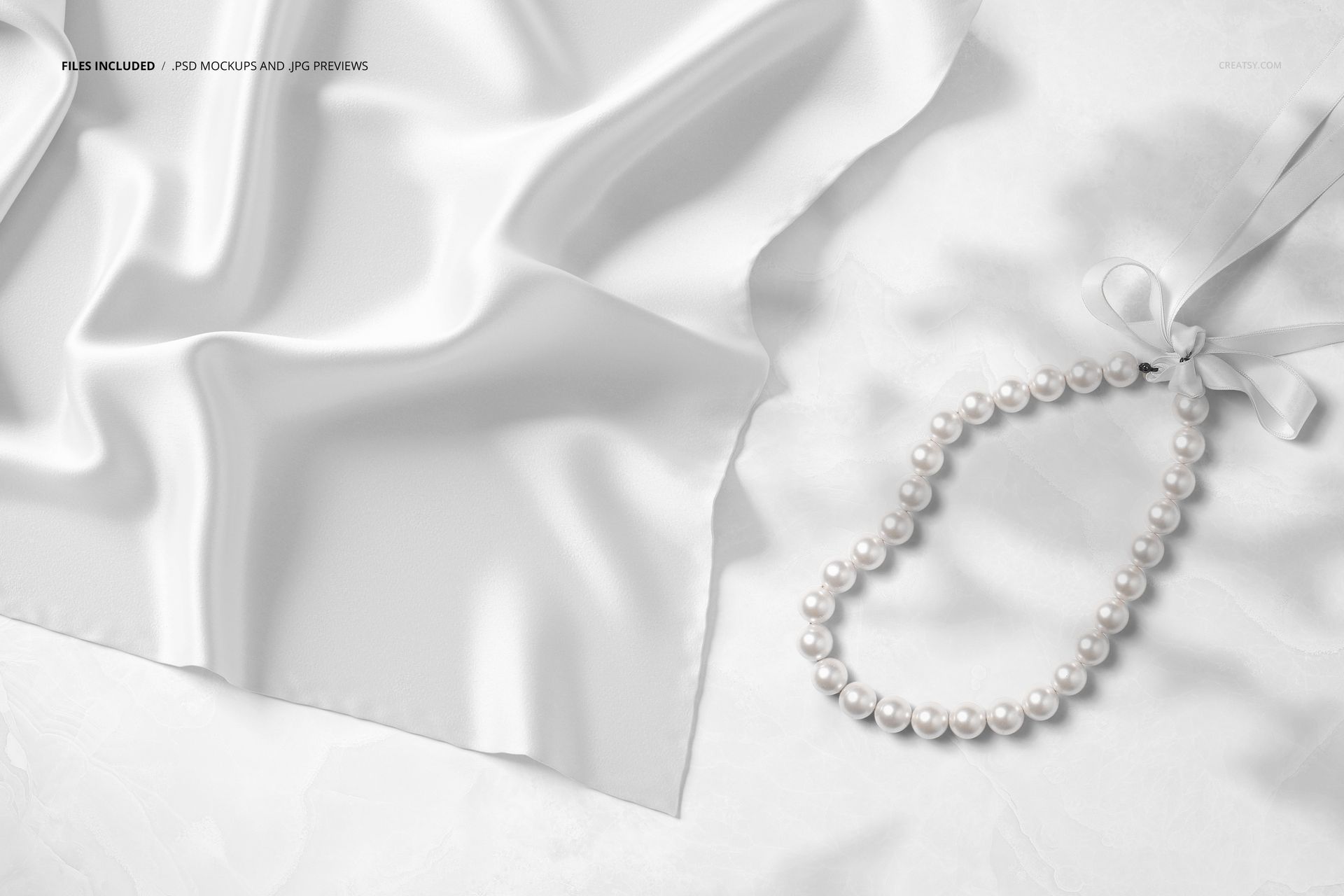 Close-up of a white silk scarf mockup displayed on a marble surface with a pearl necklace and ribbon beside it.