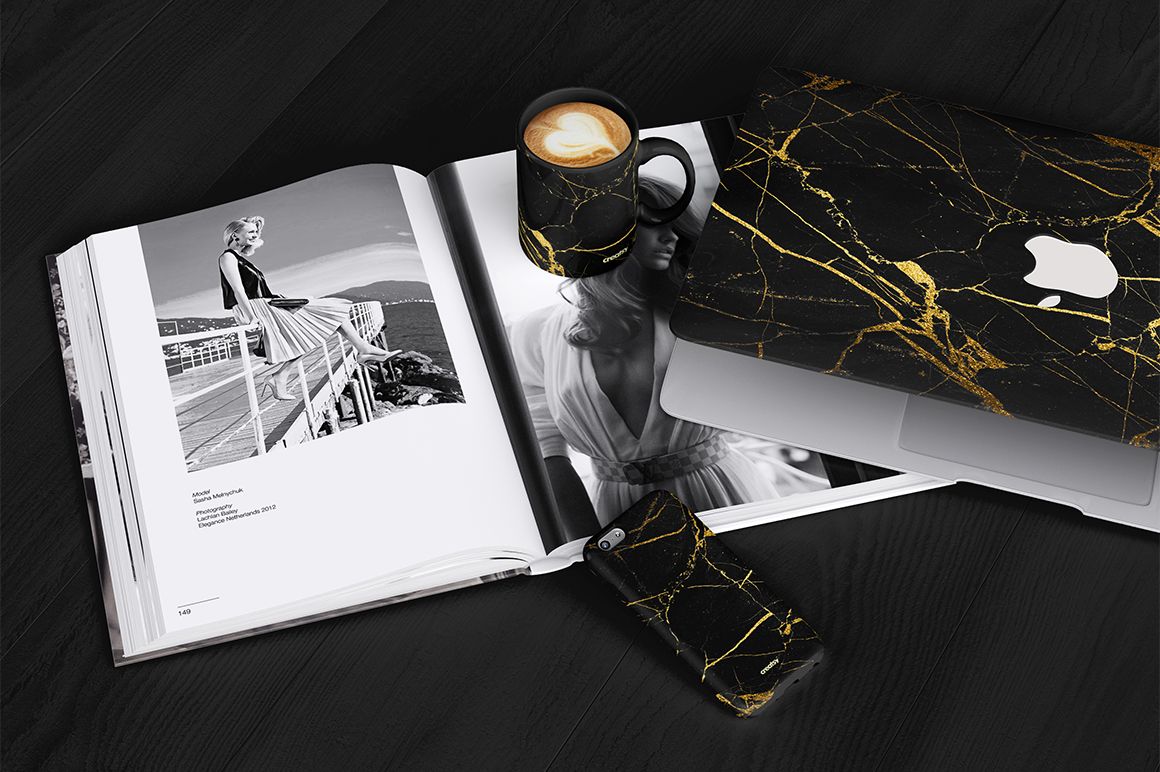 PSD mockup scene featuring a black marble mug, phone case, and laptop case with gold accents arranged on a table.