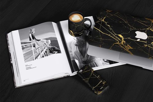 PSD mockup scene featuring a black marble mug, phone case, and laptop case with gold accents arranged on a table.