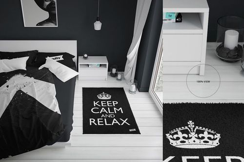 PSD mockup of a black rug with white lettering and crown motif, displayed on a white floor next to a nightstand.