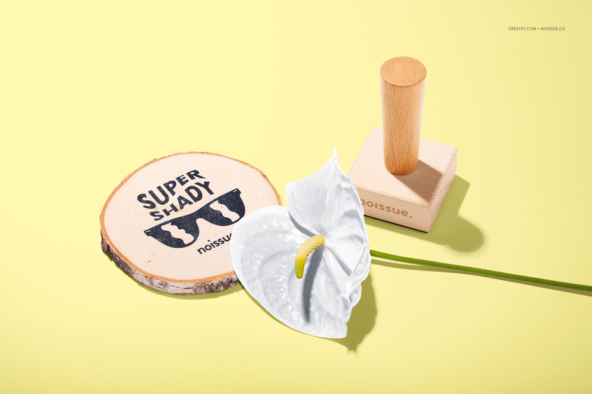 Stationery mockup featuring a wooden stamp, stamped round wood piece, and white flower on a light yellow backdrop.