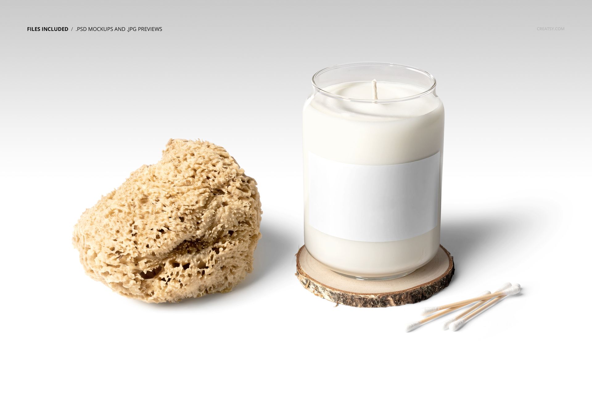Glass candle mockup with blank label, white wax, placed beside a textured sponge and three cotton swabs on white surface.