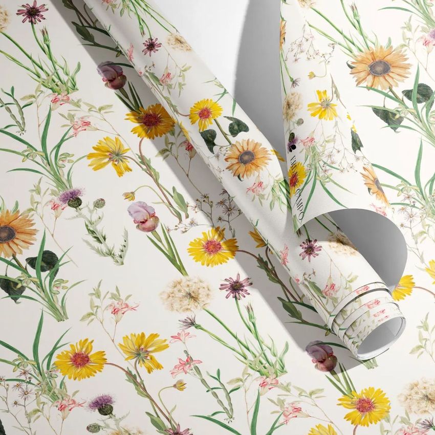 Gift wrapping paper mockup showing rolled and unrolled sheets with a botanical floral pattern on a light background.