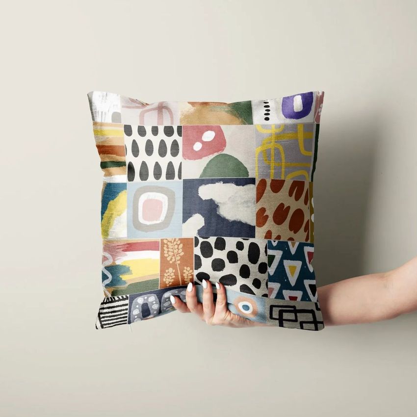Hand holding a polyester cushion cover mockup featuring a colorful patchwork design with abstract patterns and shapes.