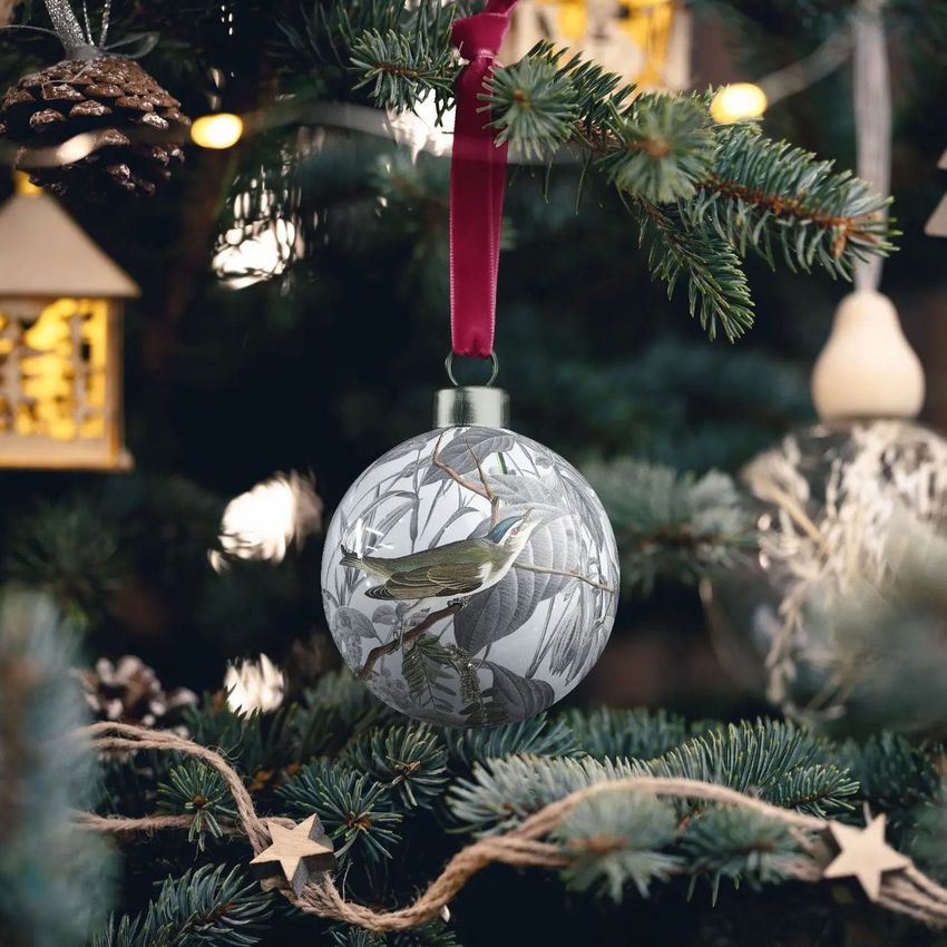 Handmade bone china Christmas bauble mockup hanging on a decorated tree, featuring a bird illustration and red ribbon.