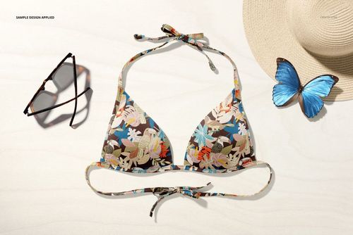 Floral patterned bikini top mockup displayed from above on a light surface, with sunglasses, straw hat, and blue butterfly nearby.