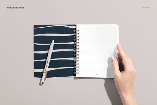 Little notebook mockup showing front view of spiral binding, patterned cover, and blank lined pages beside a pen.