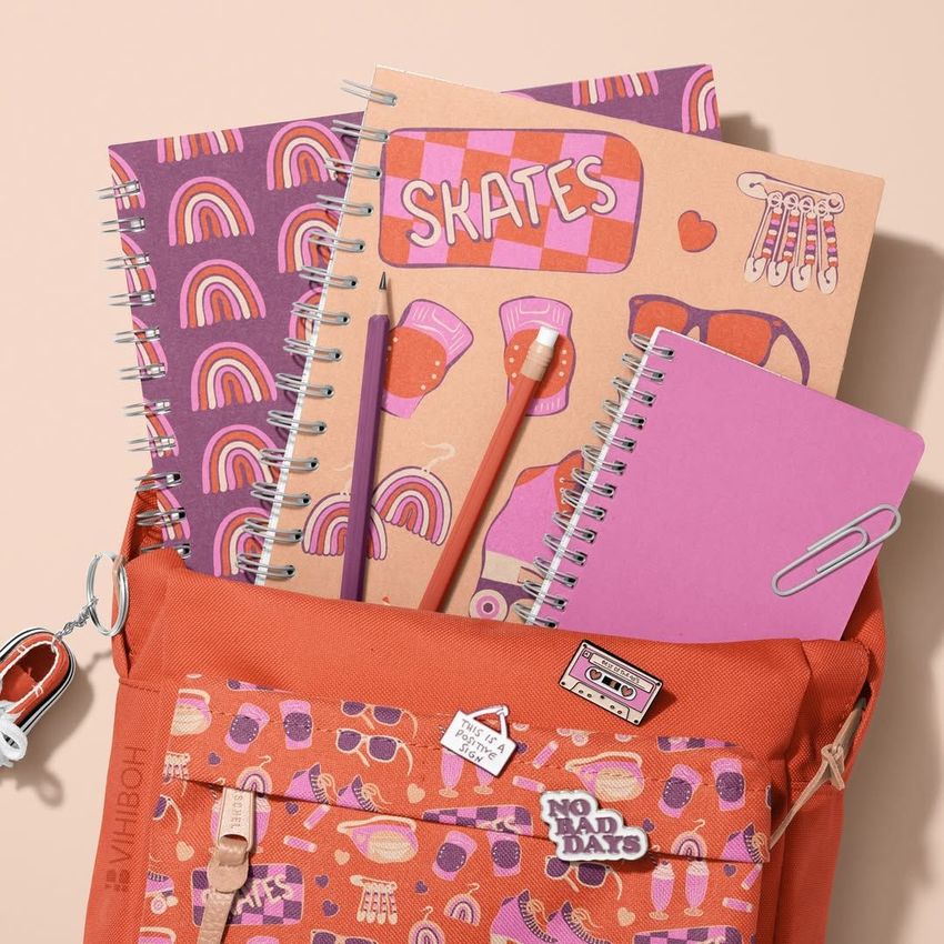 School backpack mockup in orange with spiral notebooks featuring colorful rainbow and roller skate patterns, shot from above.