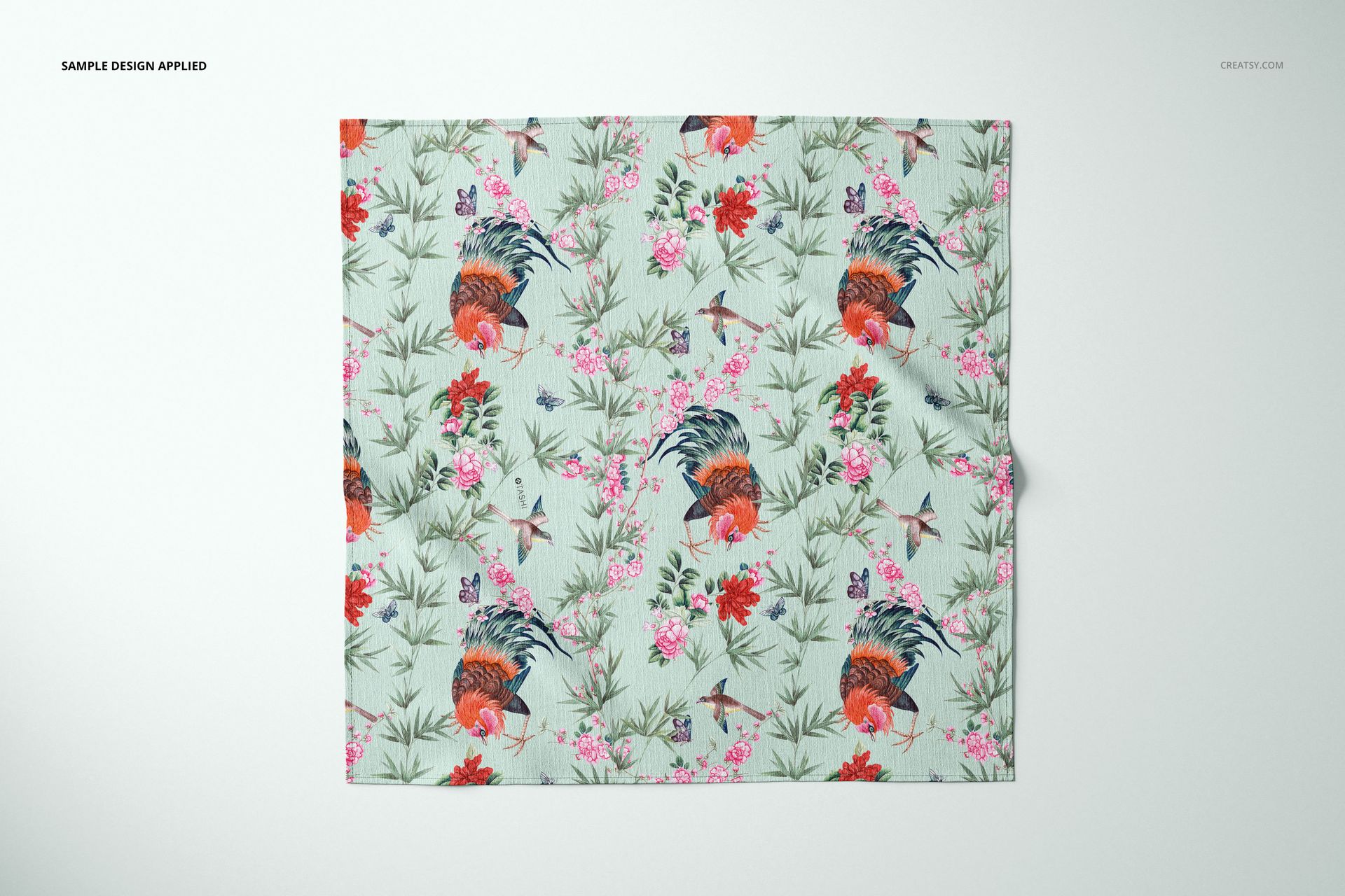 Furoshiki fabric mockup showing a flat square textile with birds, flowers, and greenery in a repeating pattern.