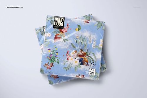 PSD mockup showing decorative napkins with a colorful floral and angel motif on a pale surface.