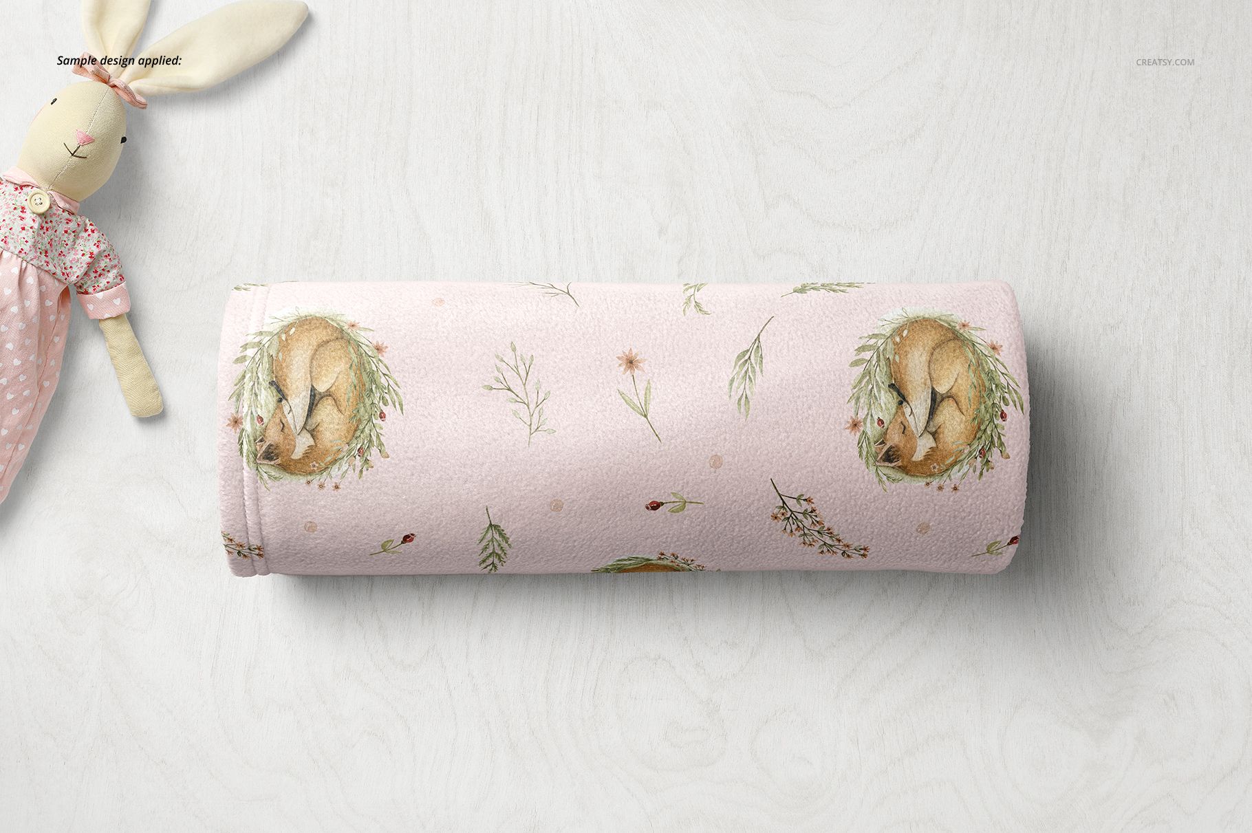 Top view of a rolled baby blanket mockup with soft fleece texture, pink color, fox and plant illustrations.