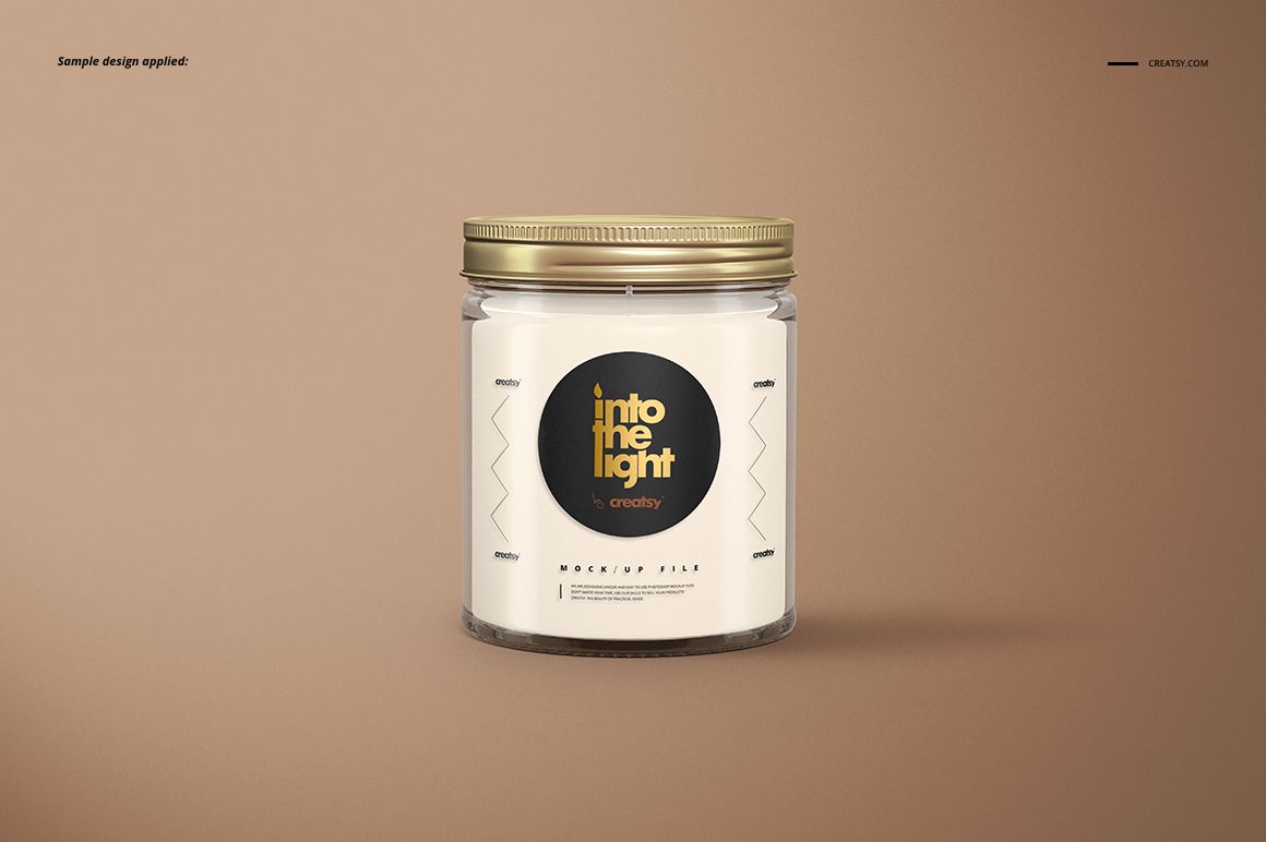 Glass jar candle mockup with a metallic gold lid and circular black label, displayed against a light brown backdrop.