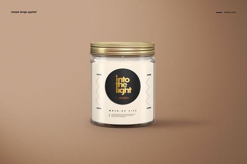 Glass jar candle mockup with a metallic gold lid and circular black label, displayed against a light brown backdrop.