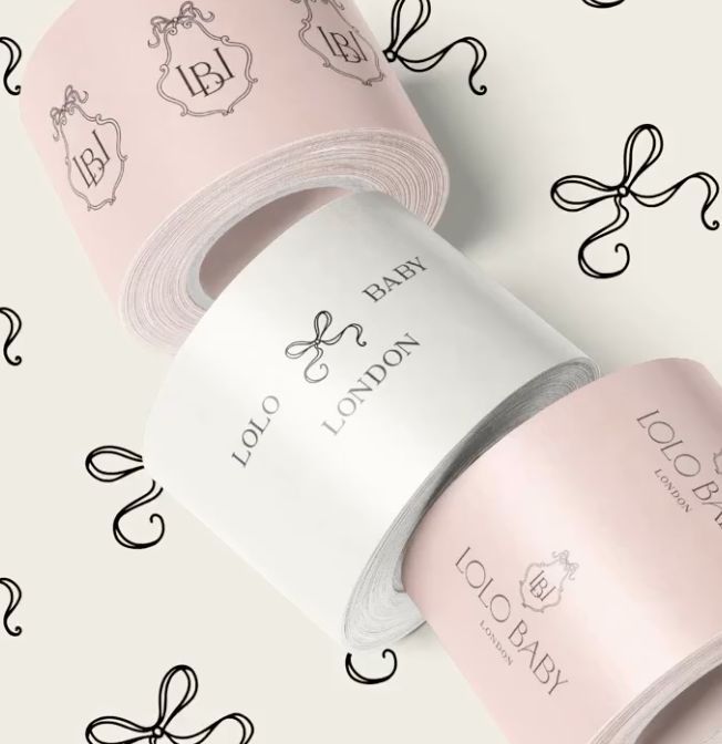Mailing box mockup featuring three rolls of custom printed paper in pastel pink and white with elegant logo designs and bow patterns.