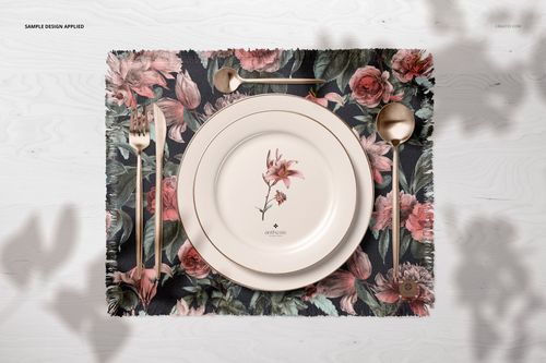 PSD mockup showing a decorative fringed placemat, floral-themed plate, and gold fork, knife, and spoon on a white wooden table.