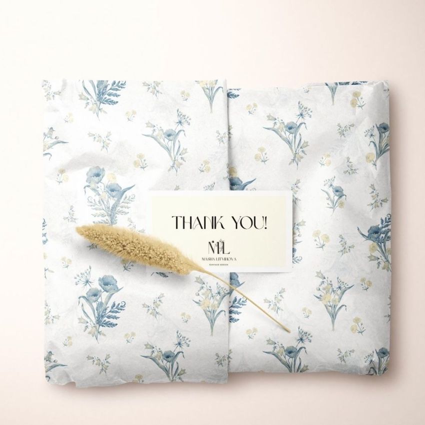 Tissue paper mockup featuring a floral pattern in soft blue and yellow tones, wrapped with a thank you card and dried grass on a light background.