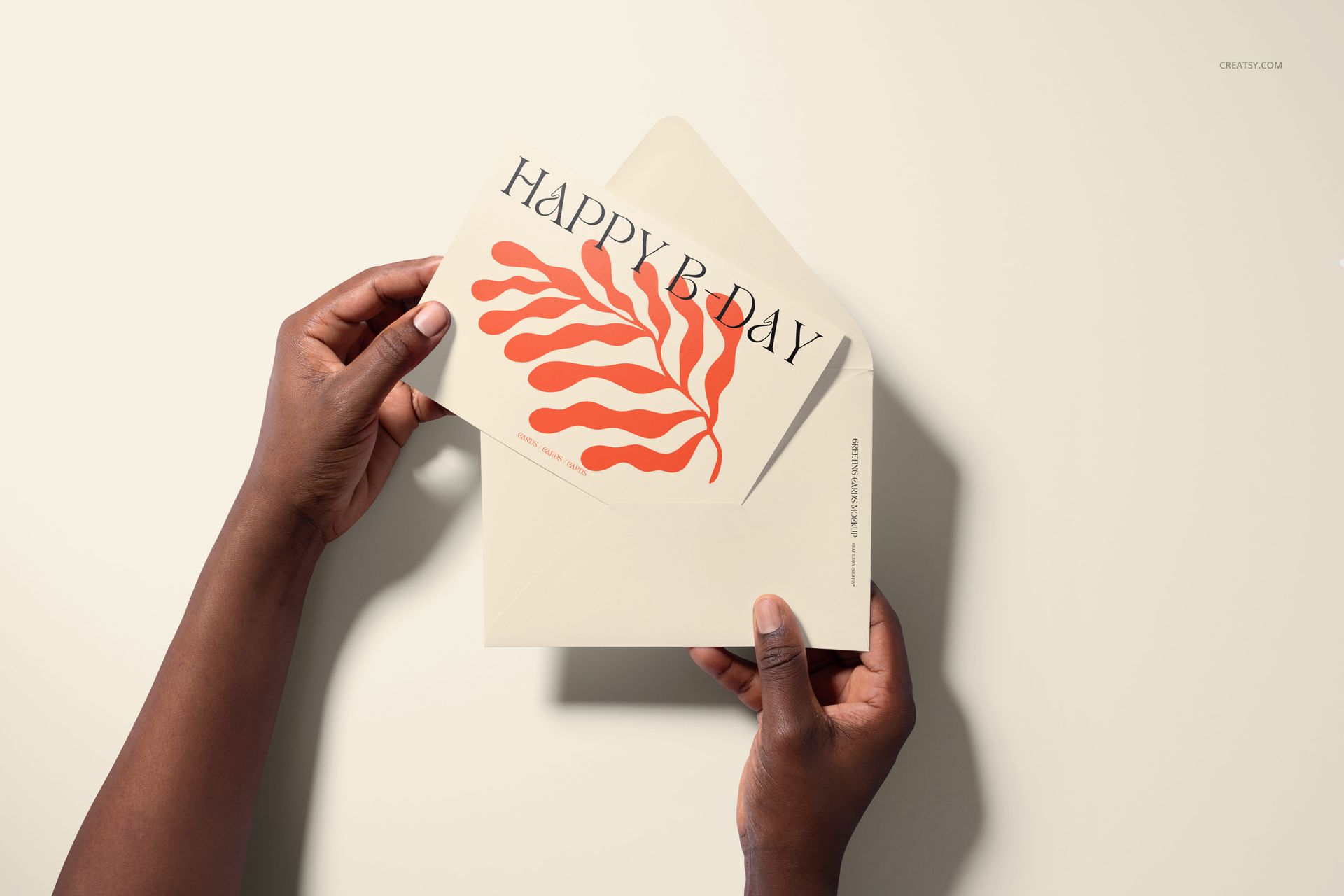 Top view of a person presenting a 5x7 greeting card mockup with orange botanical artwork and large black lettering.