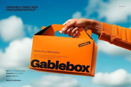Front view of a bright orange gable box held by a hand against a blue sky background, used for branding mockups.