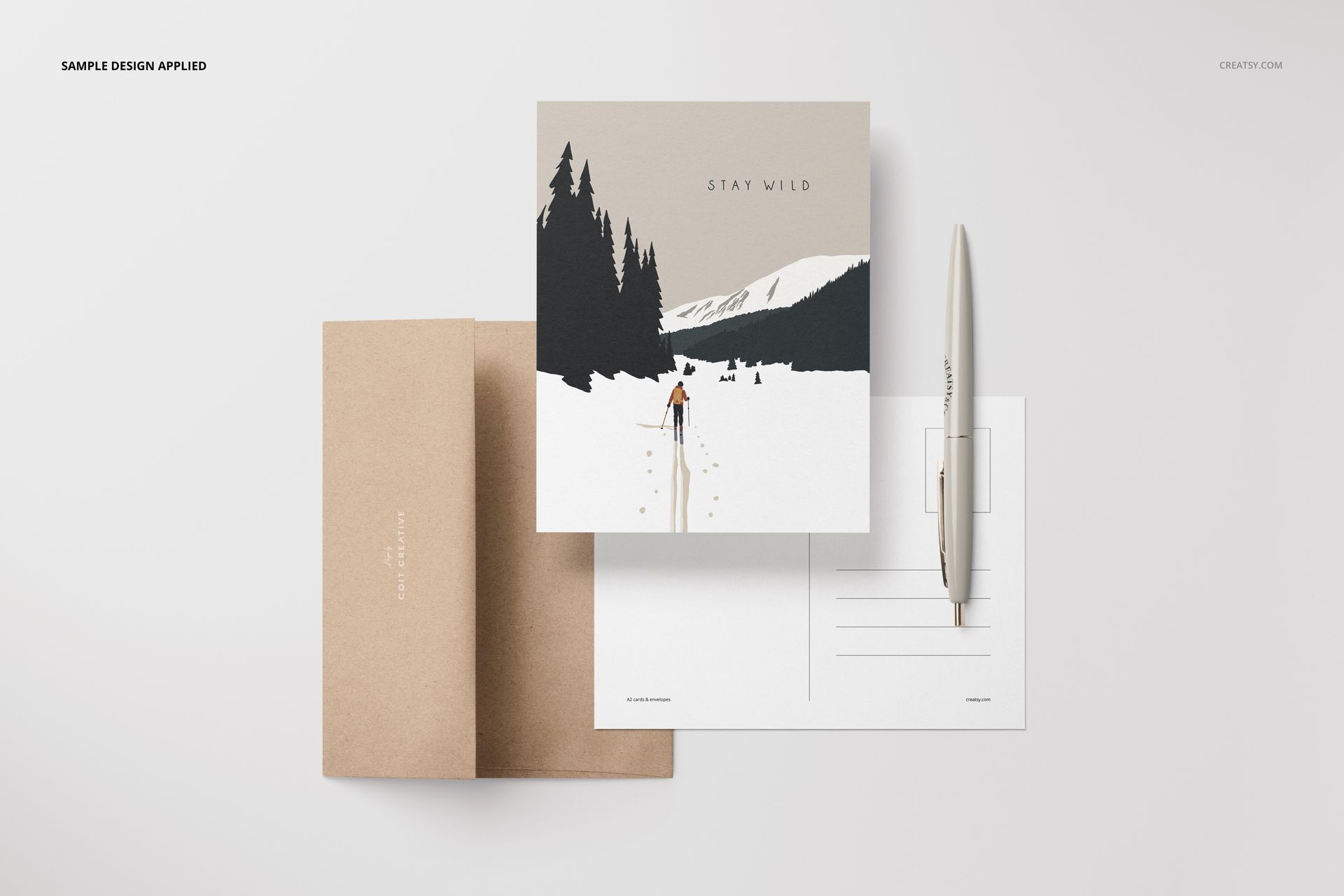 A2 card mockup set with a front view of a square card featuring a mountain scene, brown envelope, and pen on a white surface.