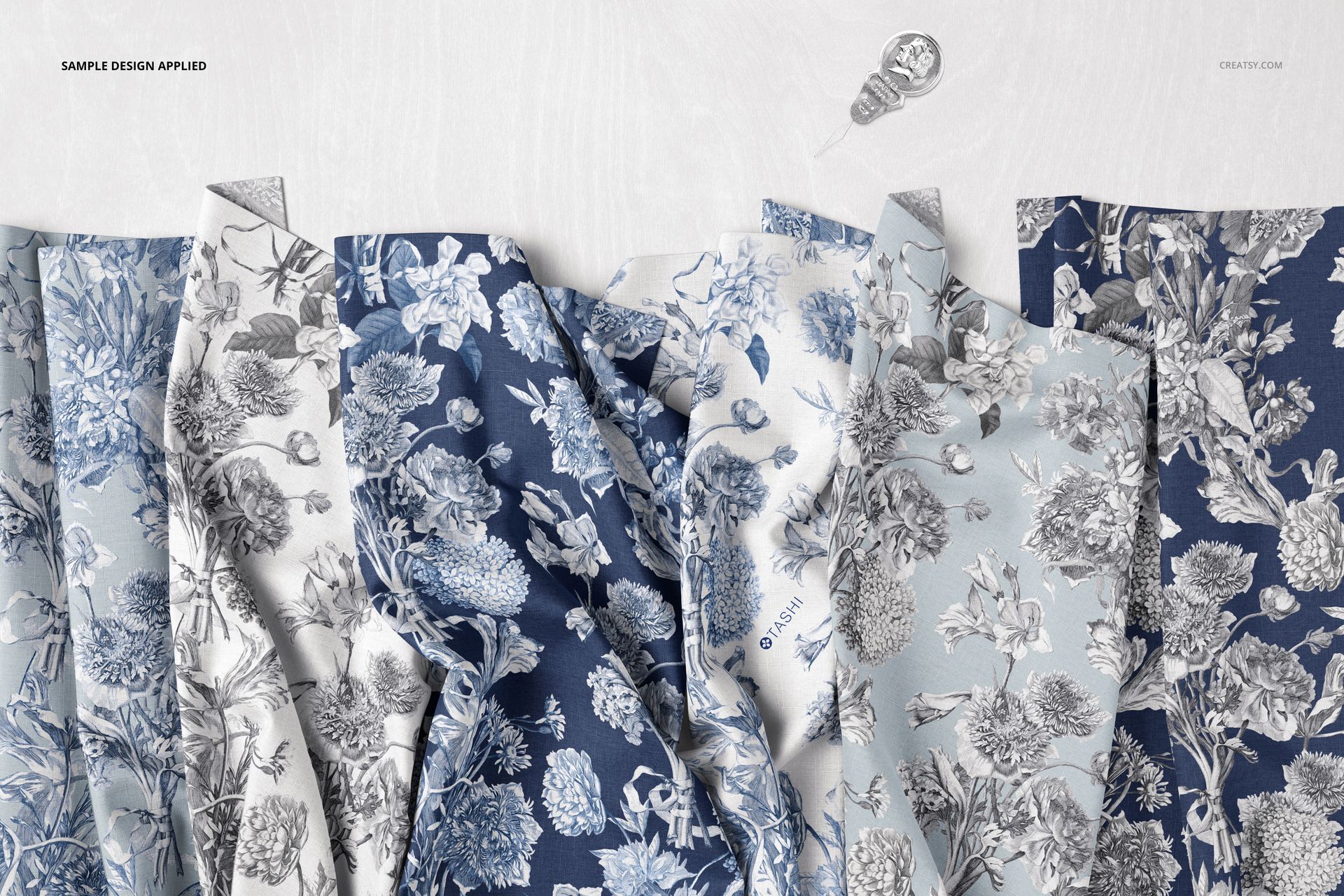 PSD mockup showing multiple folded fabric samples with detailed botanical prints in cool colors, viewed from above.