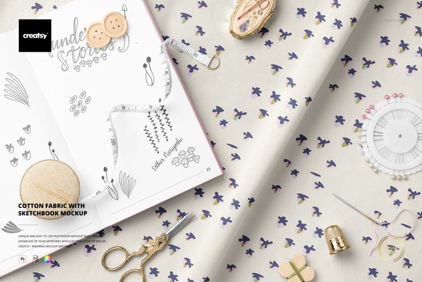 Top view of cotton fabric mockup featuring a subtle floral print, sketchbook with drawings, and various sewing accessories.