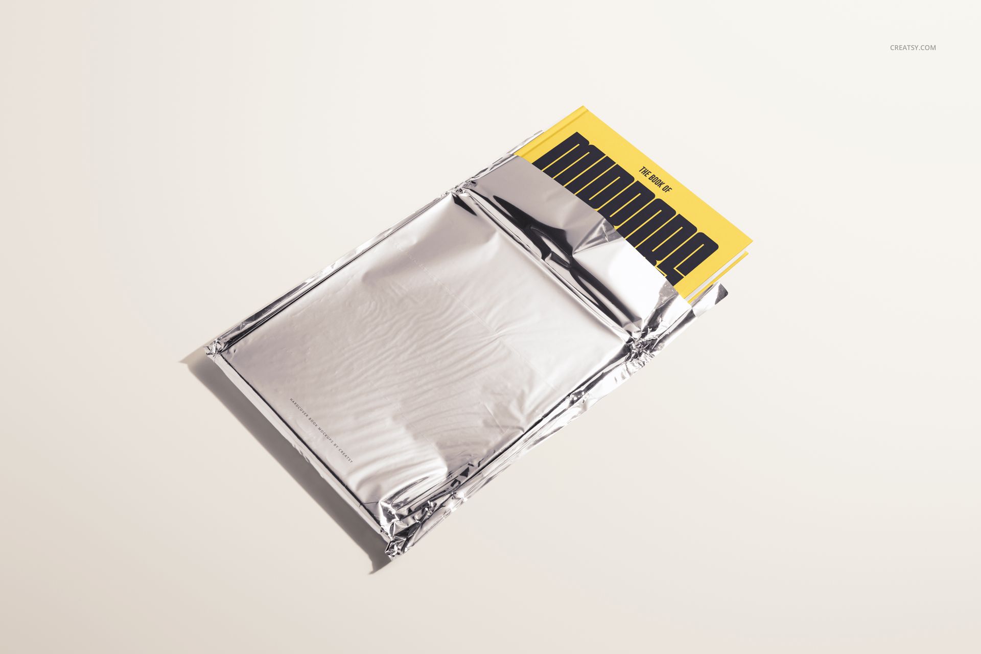 Yellow hardcover book mockup set in metallic foil packaging, shown from a diagonal top view on a neutral surface.