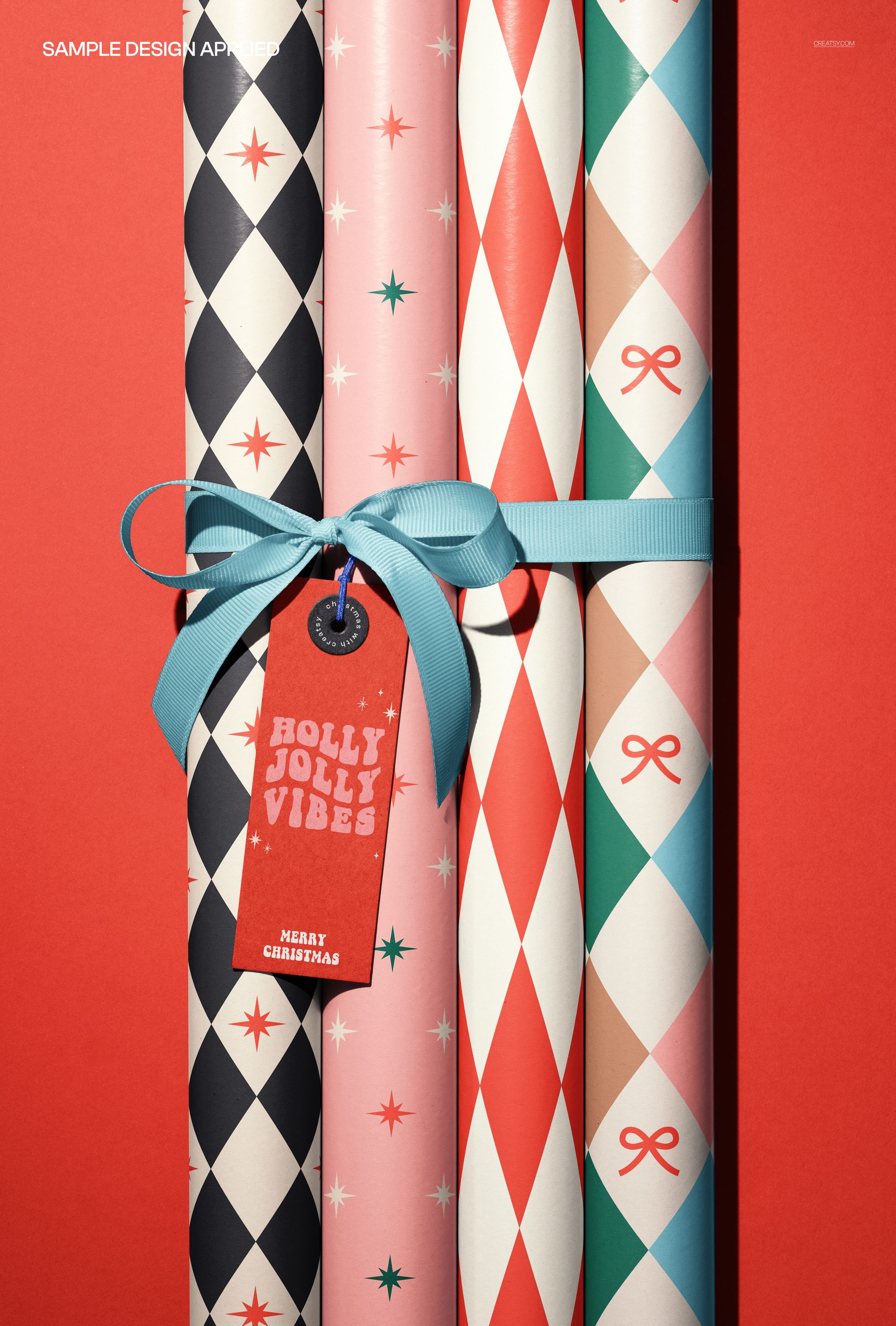 Four wrapping paper rolls with festive patterns, tied with a blue ribbon and a red paper tag, front view mockup.
