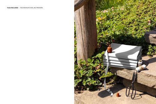 PSD mockup showing a pile of neatly folded fabric on rustic garden steps, accompanied by sewing accessories and foliage.