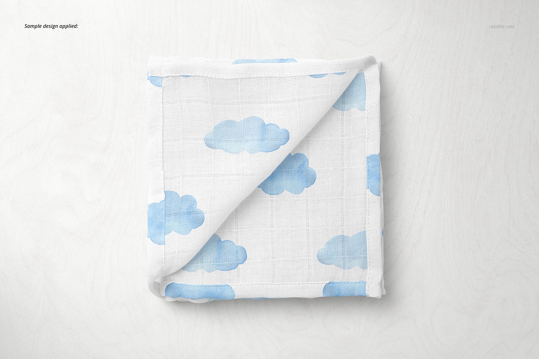 Baby muslin square nappy mockup featuring soft white material with blue clouds, displayed folded on a pale background.